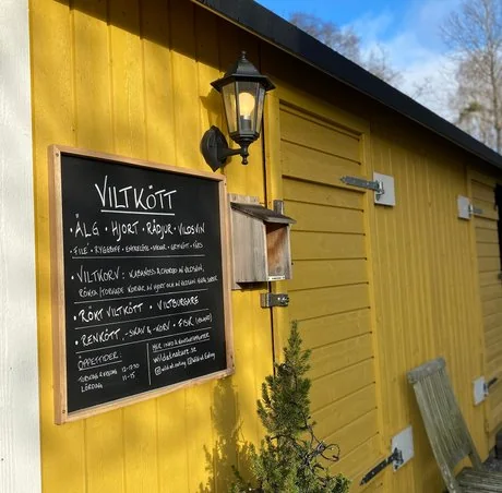 Gårdsbutikens gula fasad med handskriven viltkött-skylt: älg, hjort, rådjur, vildsvin